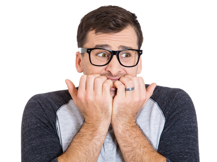 Closeup portrait of nervous, stressed young nerdy guy man with eyeglasses biting fingernails looking anxiously craving something isolated on white background. Negative emotion expression feeling