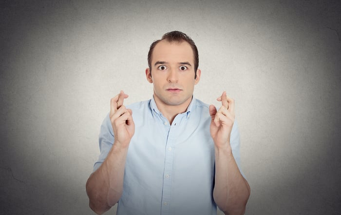 Closeup portrait young funny looking guy, sarcastic, anxious business man crossing fingers, wishing, hoping for luck, miracle isolated grey wall background. Emotions, facial expressions, feelings