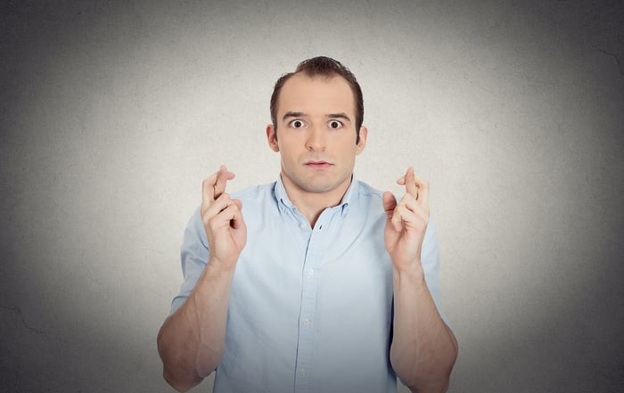Closeup portrait young funny looking guy, sarcastic, anxious business man crossing fingers, wishing, hoping for luck, miracle isolated grey wall background. Emotions, facial expressions, feelings